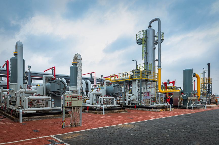 Wide-angle view of a modern natural gas processing plant featuring complex piping networks and industrial vessels under a cloudy sky.