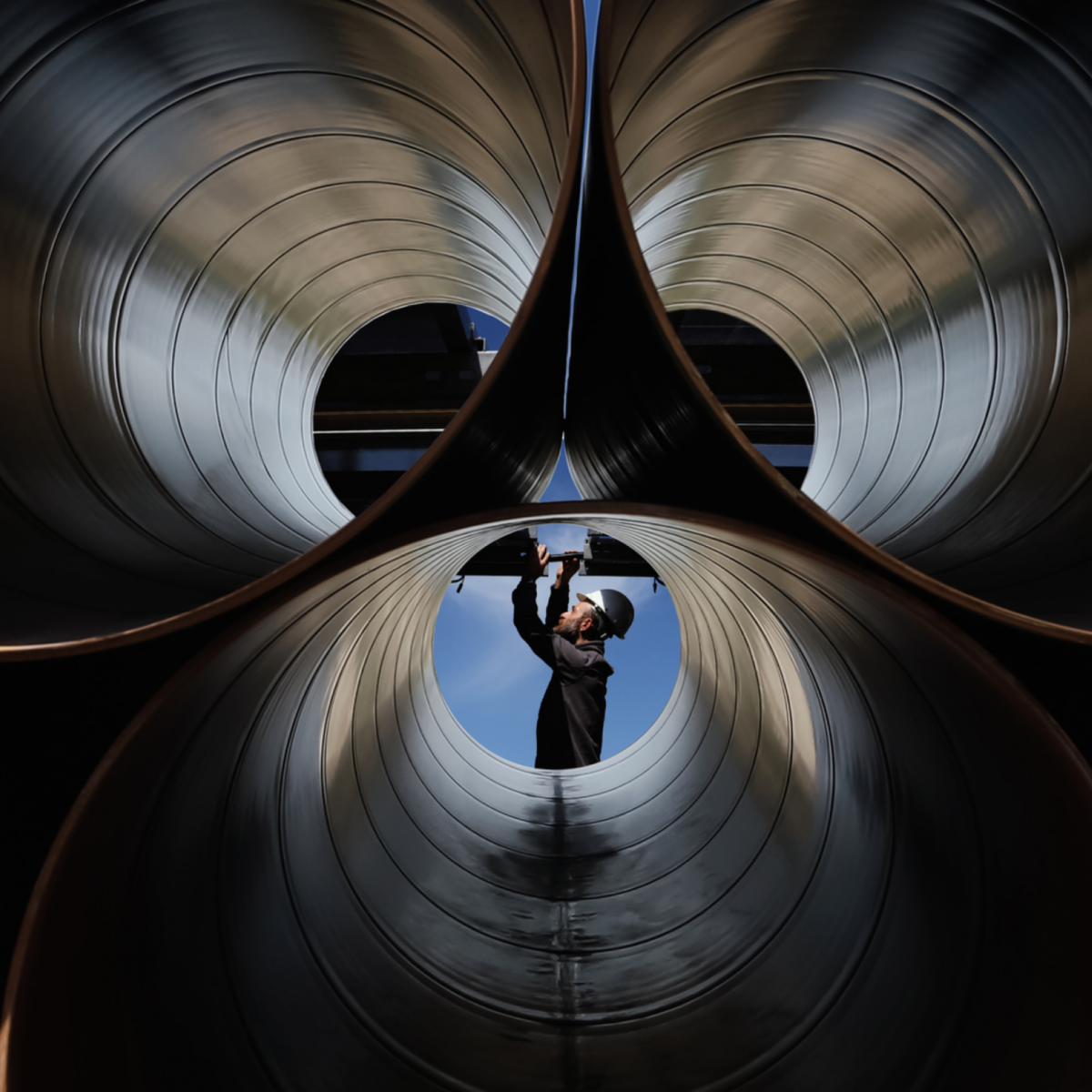 Worker inspecting large industrial pipes, representing heat transfer systems, energy efficiency, and advanced mechanical engineering solutions.