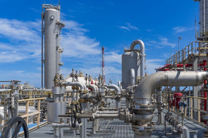 Stainless steel pipes, valves, and industrial towers stand under a bright blue sky at a modern chemical processing facility.