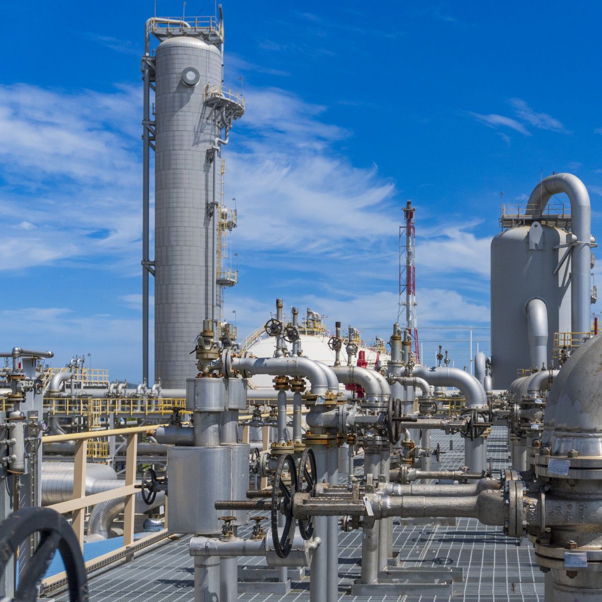 Stainless steel pipes, valves, and industrial towers stand under a bright blue sky at a modern chemical processing facility.