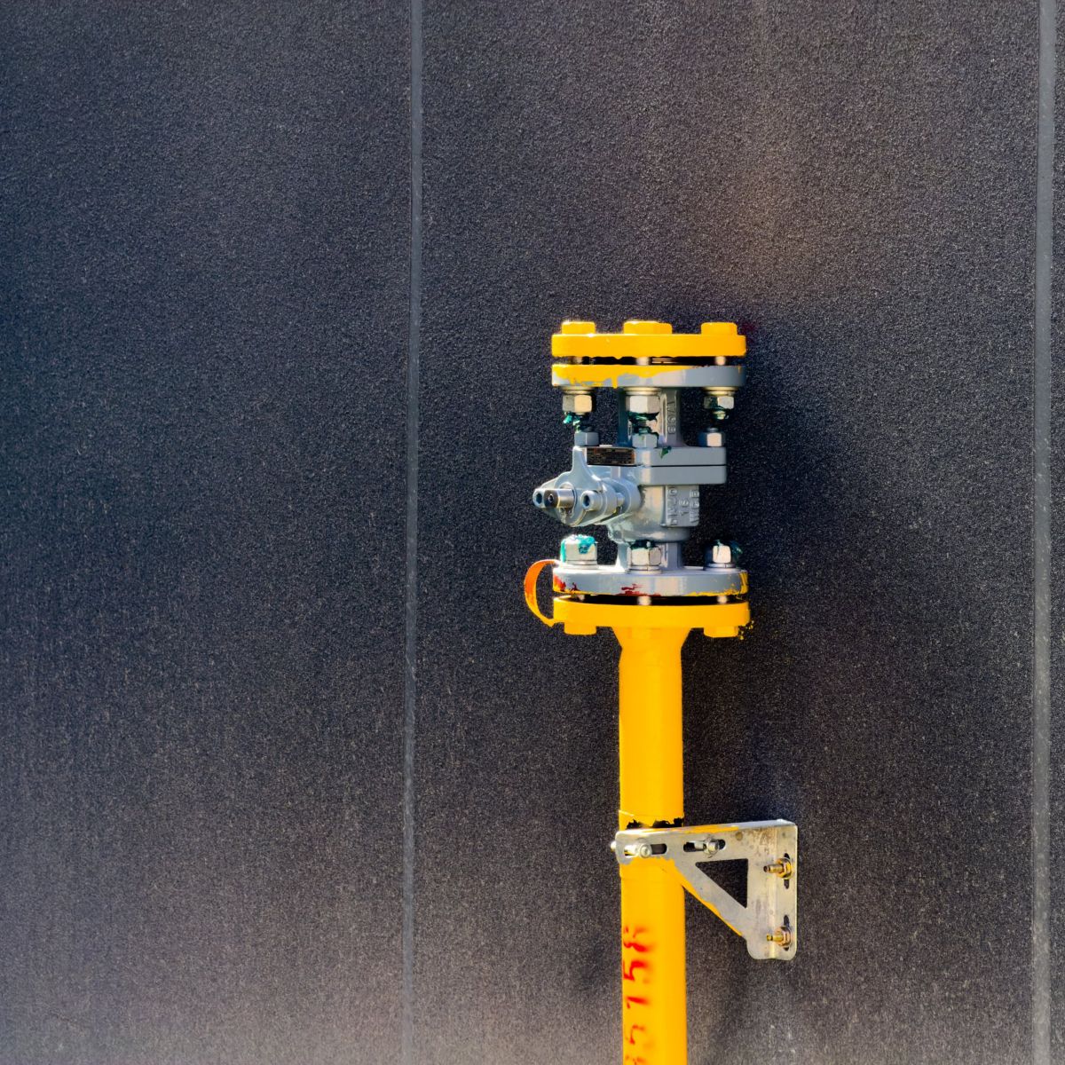 A bright yellow industrial valve stands mounted against a modern, textured dark grey wall.