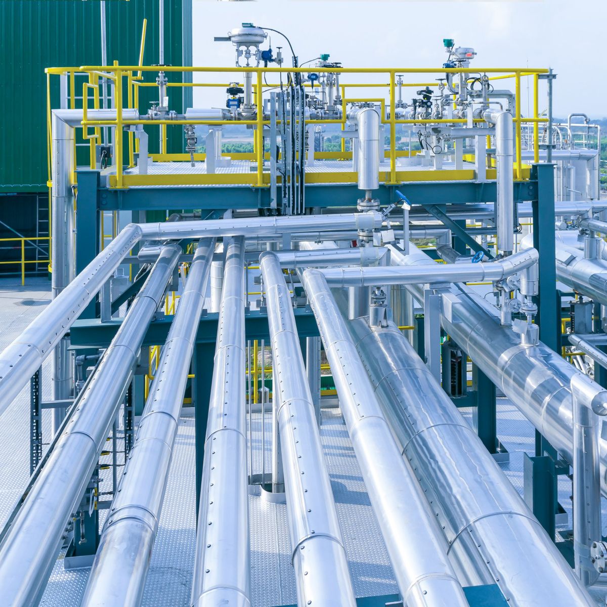 A complex network of stainless steel pipes and valves forms the modern processing equipment at an industrial refinery site.