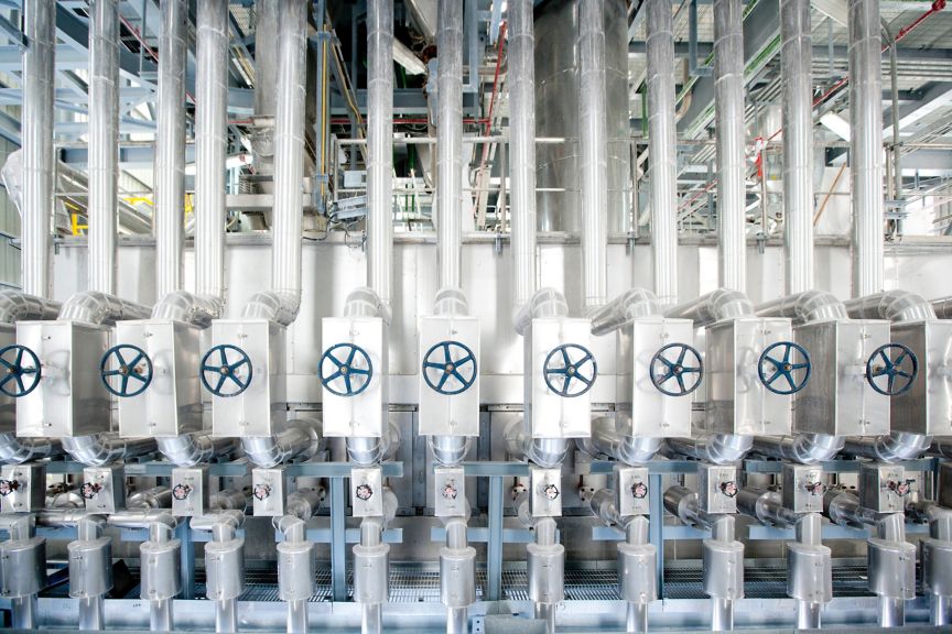 A symmetrical view of industrial pipes and valve wheels in a chemical manufacturing facility.