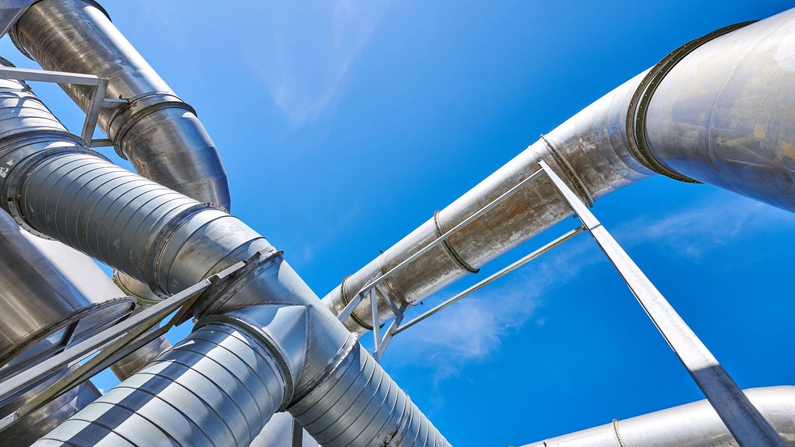 A close-up view of metallic pipes intersecting under a bright blue sky, showcasing industrial engineering.