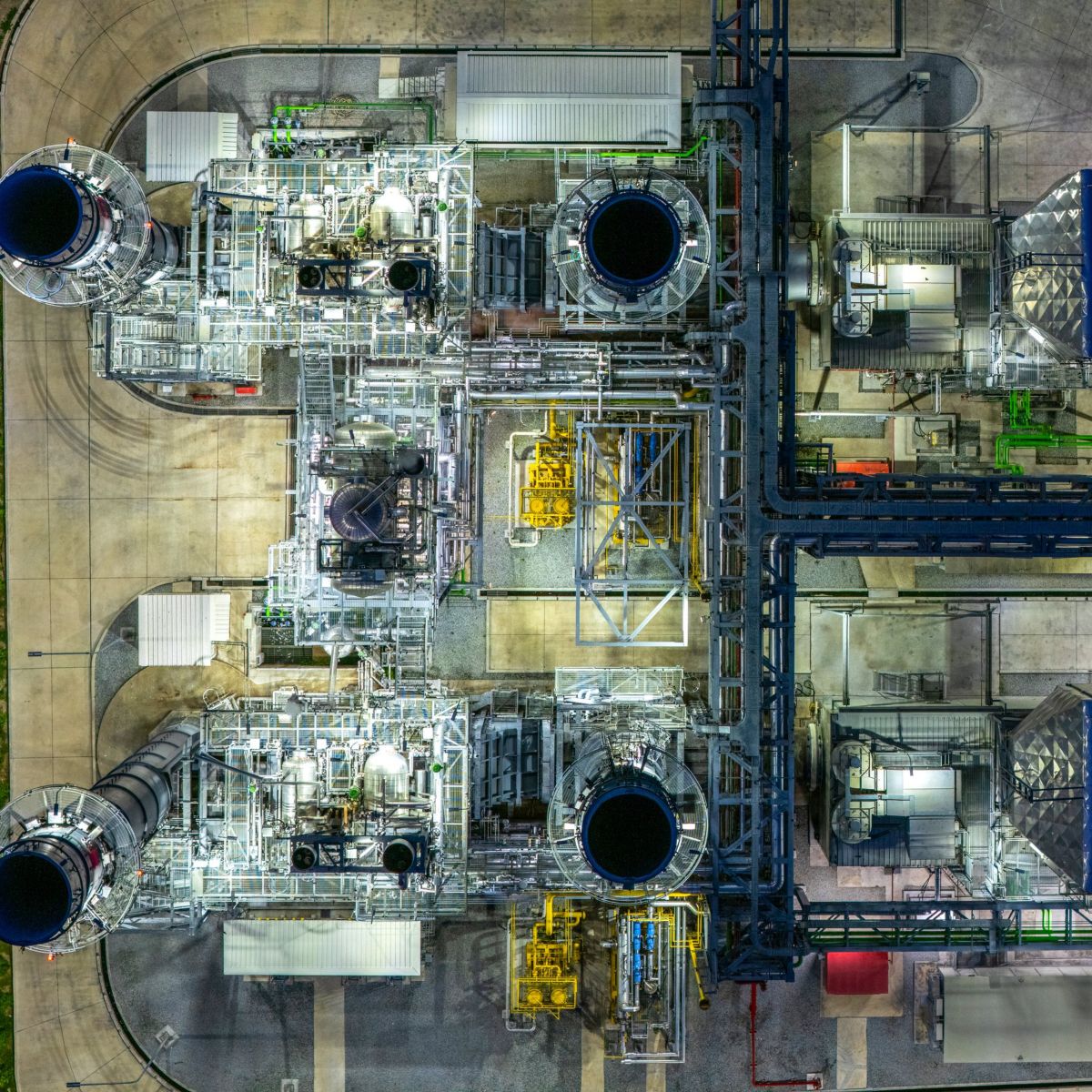 Overhead drone perspective of a modern power plant illuminated at night, highlighting complex structural machinery and pipeline systems.