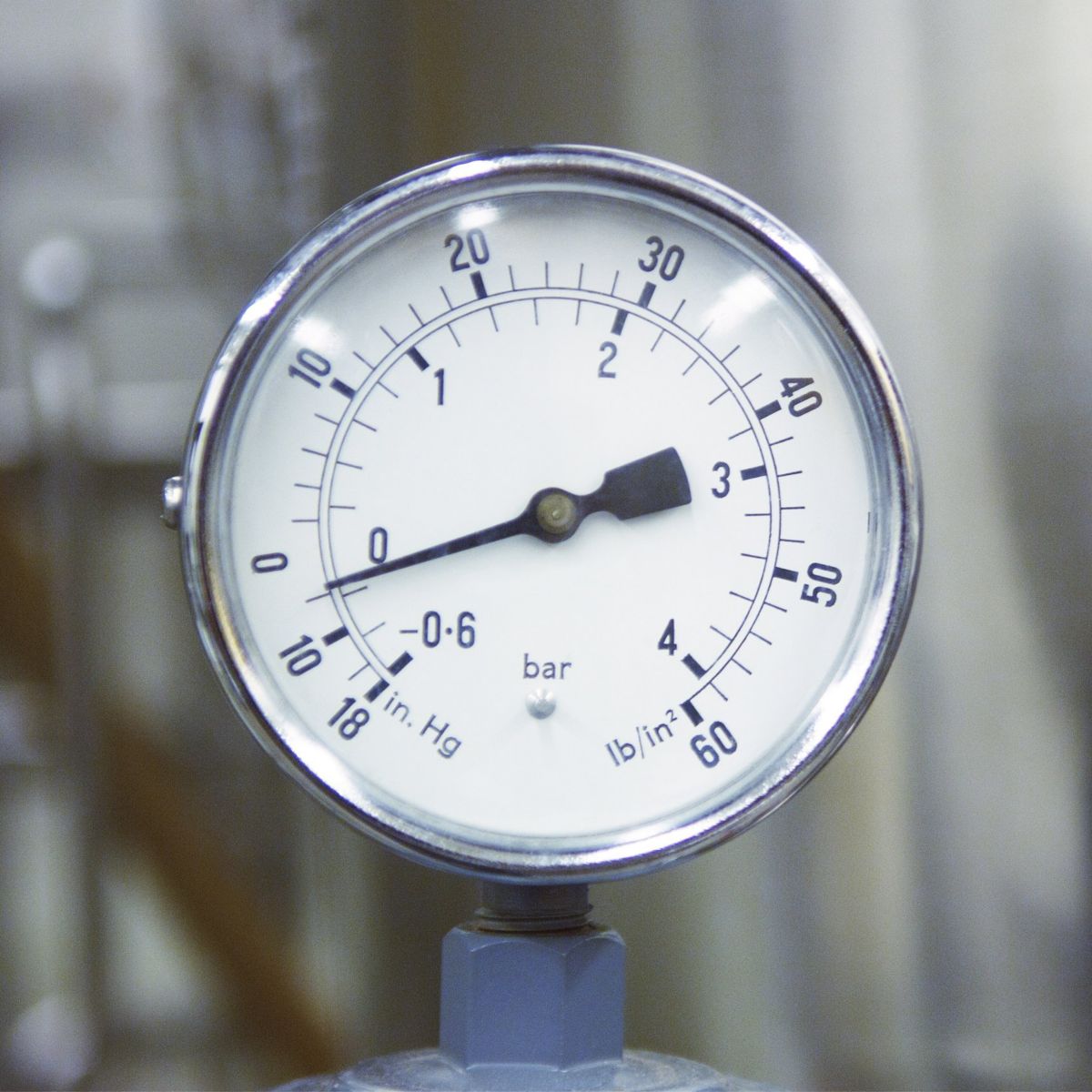 A close-up view of an analog pressure gauge measuring industrial equipment settings in bar and inches of mercury.