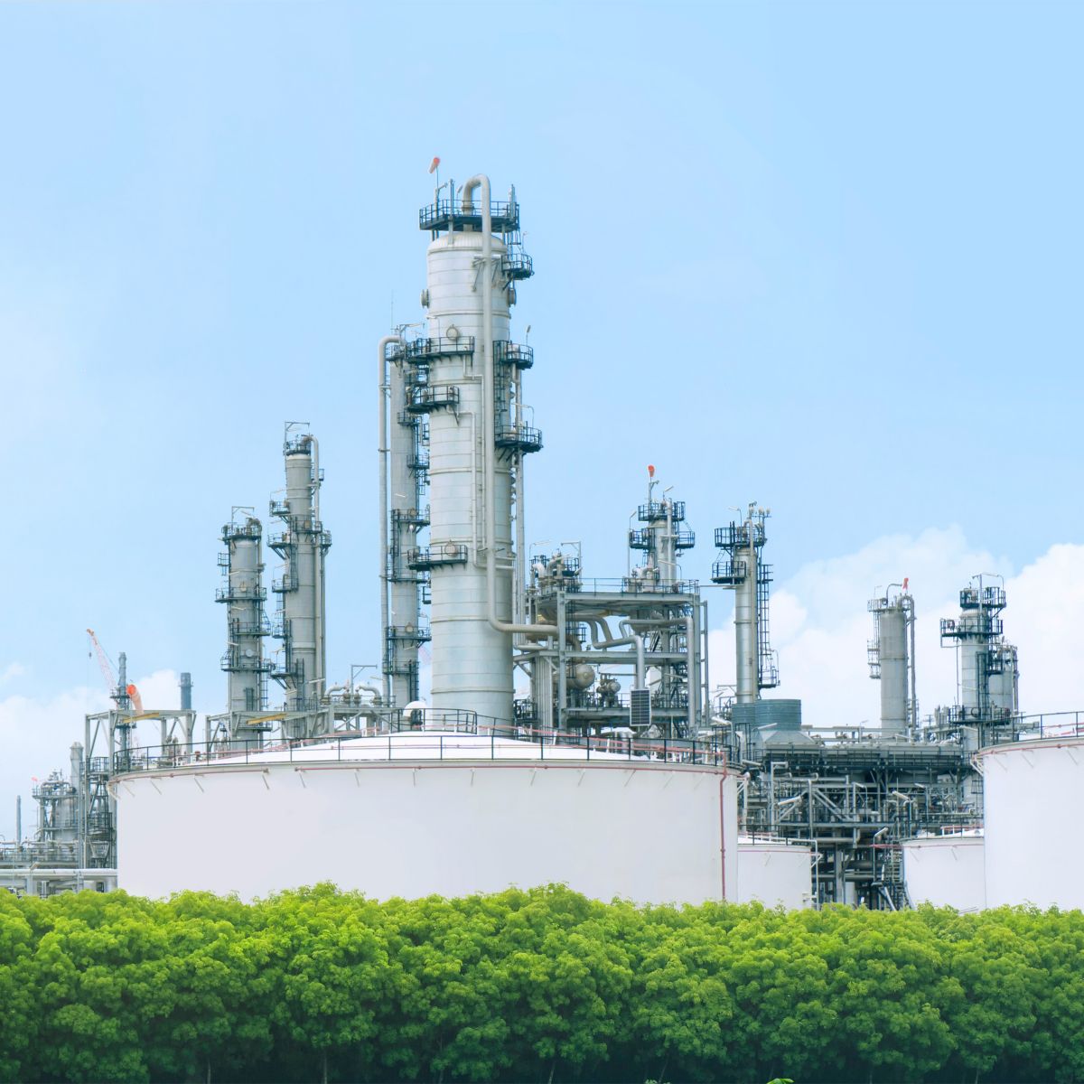 Industrial processing facility with tall distillation towers, storage tanks, pipes, and chimneys under a blue sky.