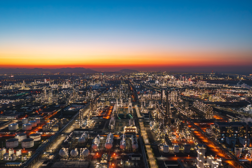 Panoramic view of a refinery facility illuminated at dusk, showcasing large-scale industrial operations, energy production, and infrastructure at night.