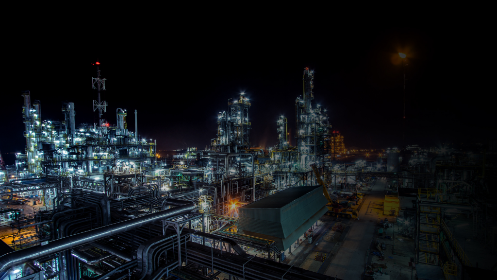 Nighttime view of an industrial refinery facility with illuminated processing units, piping networks, and operational infrastructure.