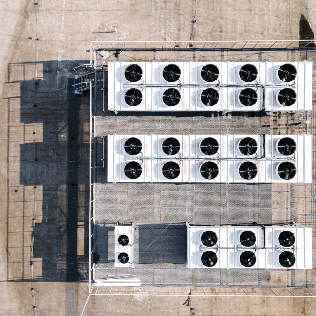 Top view of rooftop cooling units with multiple circular fans, metal structures, and blue piping on a concrete surface.