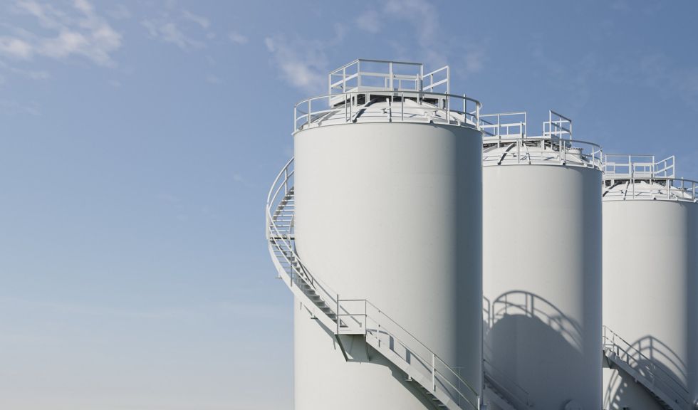 Three identical white industrial silos featuring external spiral staircases against a clear blue sky.