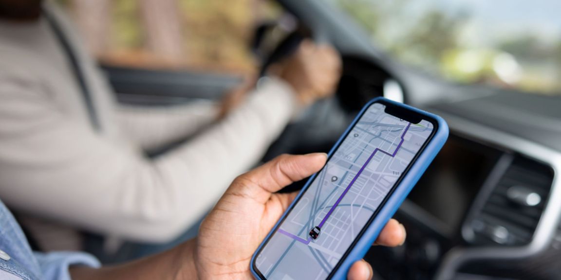 A person in the car holds a phone with a navigation map application.
