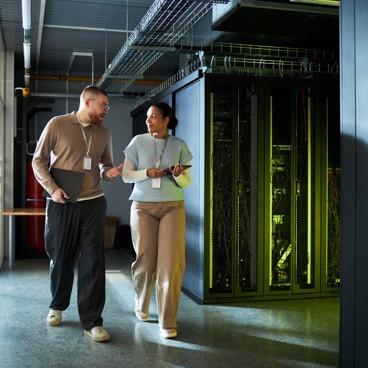 Two professionals discuss data center operations while walking through a high-tech server room aisle.