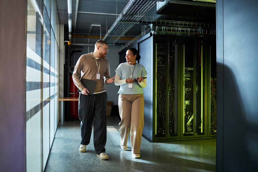 Two professionals discuss data center operations while walking through a high-tech server room aisle.