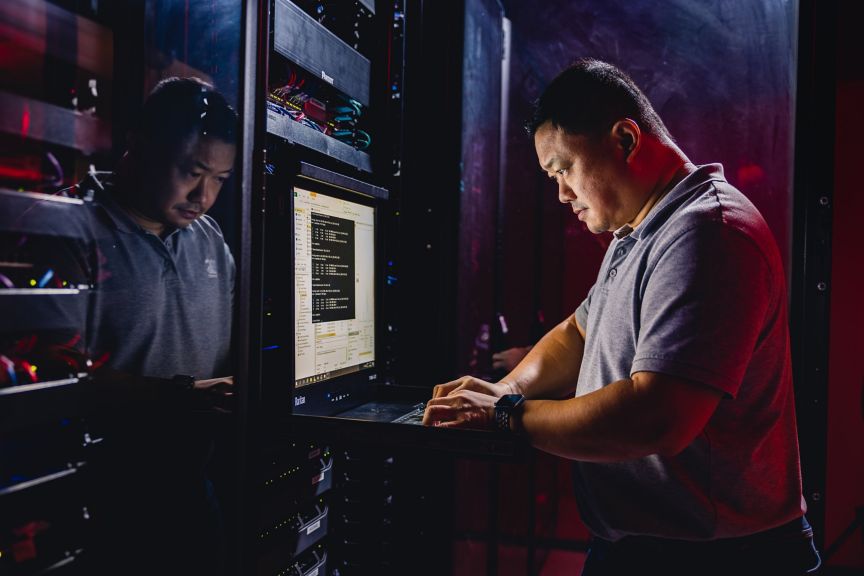 A focused technician works on a server rack console within a high-tech data center environment illuminated by atmospheric red and blue lighting.