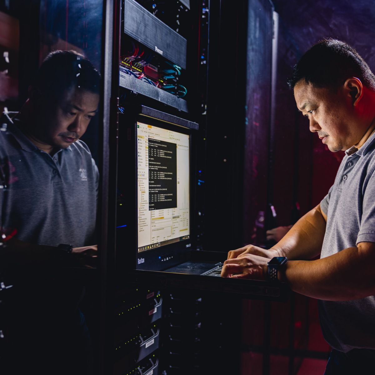 A focused technician works on a server rack console within a high-tech data center environment illuminated by atmospheric red and blue lighting.