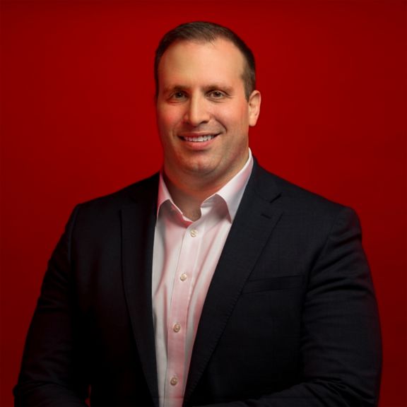Professional portrait of Jim Masso, captured against a bold red background.