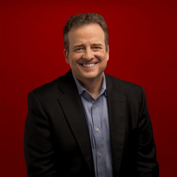 Professional portrait of Juan Picon, captured against a bold red background.