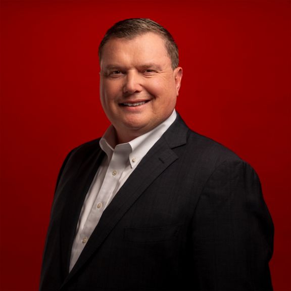 Professional portrait of Ken West, captured against a bold red background.