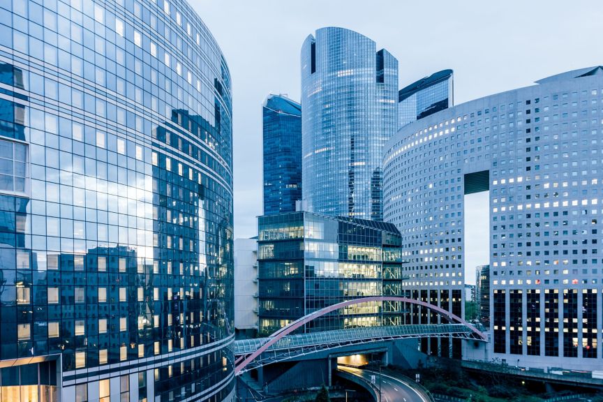 Modern high-rise architecture at La Defense in Paris, showcasing a complex urban office landscape with a pedestrian skybridge and reflective glass facades.
