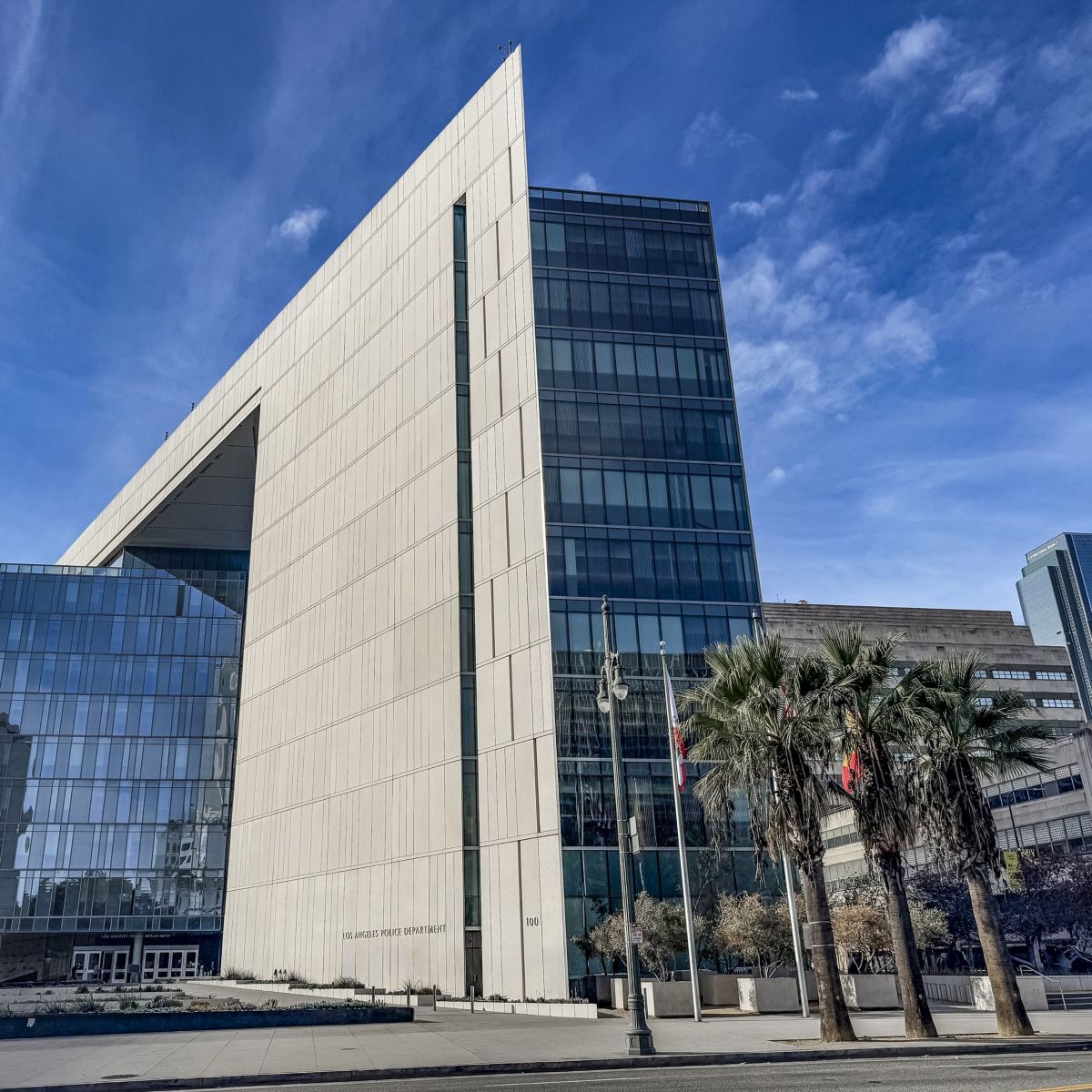 A low-angle architectural shot of the Los Angeles Police Department headquarters, emphasizing its modern glass-and-stone facade against a clear blue sky.