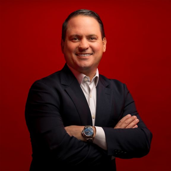 Professional portrait of Mark Macaluso, captured against a bold red background.