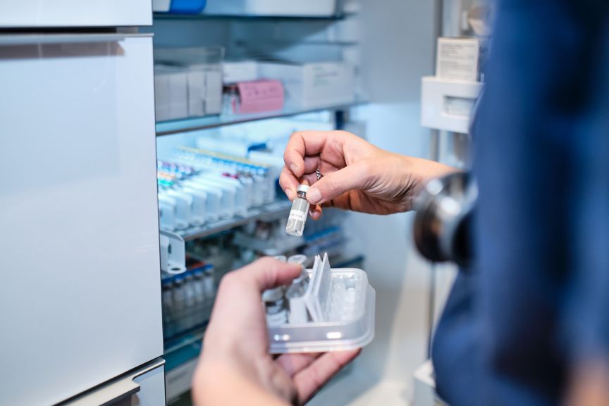 Healthcare professional retrieves a medical vial from a climate-controlled storage refrigerator.