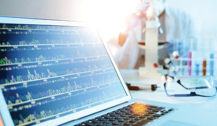 A laptop displays medical or genomic data beside laboratory equipment and sample tubes.