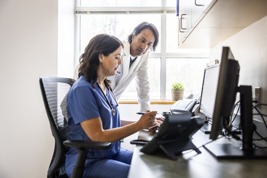 A female nurse and male doctor review digital patient charts together at a workspace.