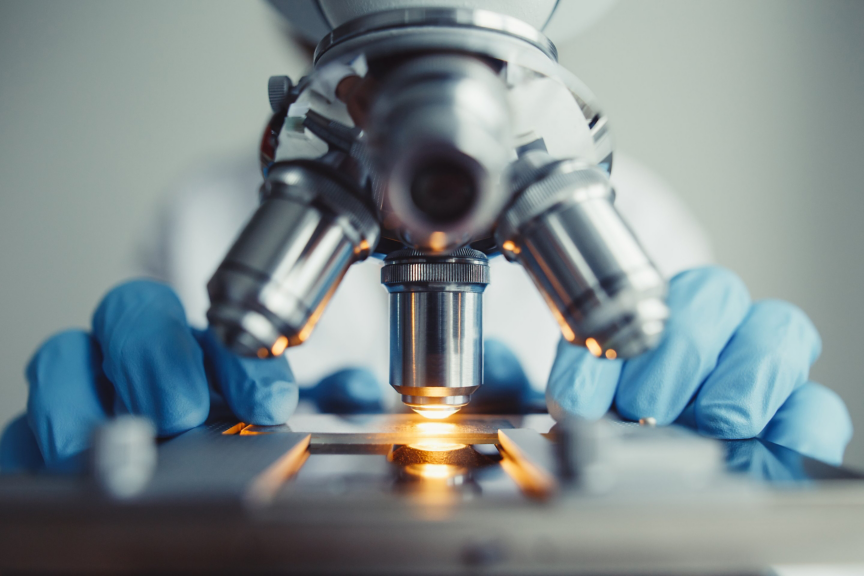 Researcher using a professional microscope with blue gloves to examine a sample in a sterile laboratory environment.
