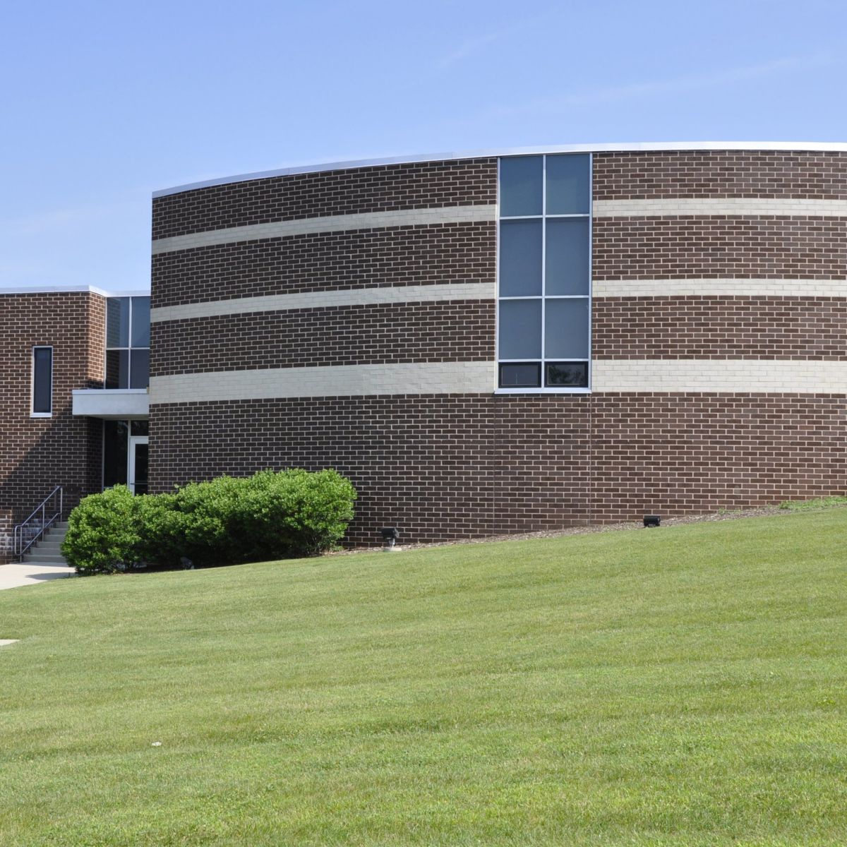 A modern brick office facility featuring curved architecture and a landscaped lawn.