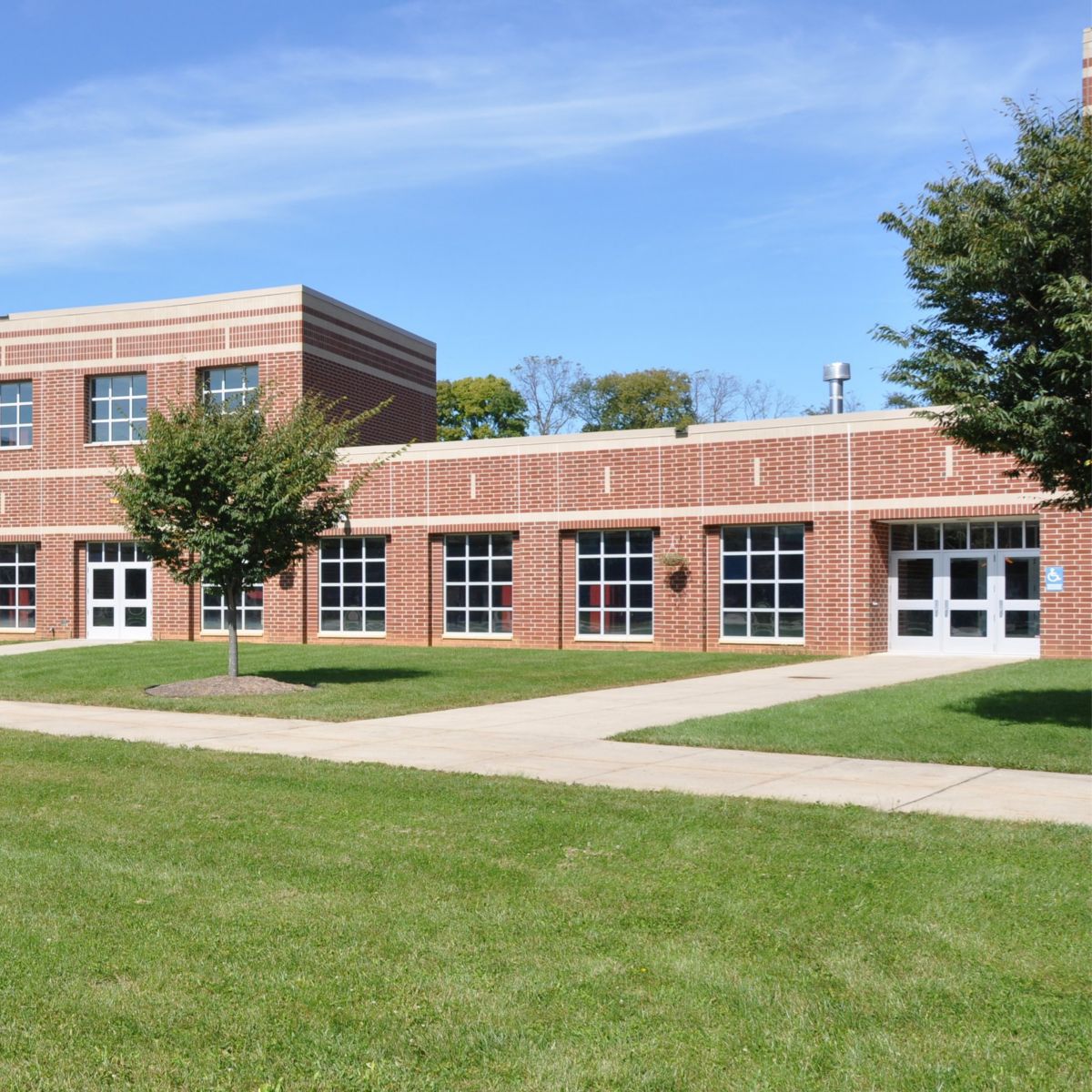 A contemporary brick school building with expansive windows set against a vibrant green lawn and clear blue sky.