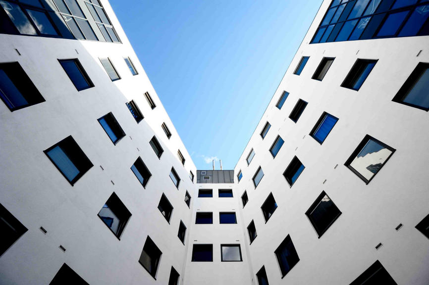 A low-angle architectural shot capturing the symmetrical white facades and dark glass windows of a modern office building against a clear blue sky.