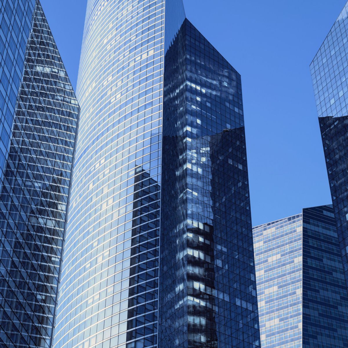 A low-angle architectural perspective of sleek glass office towers reflecting the blue sky.