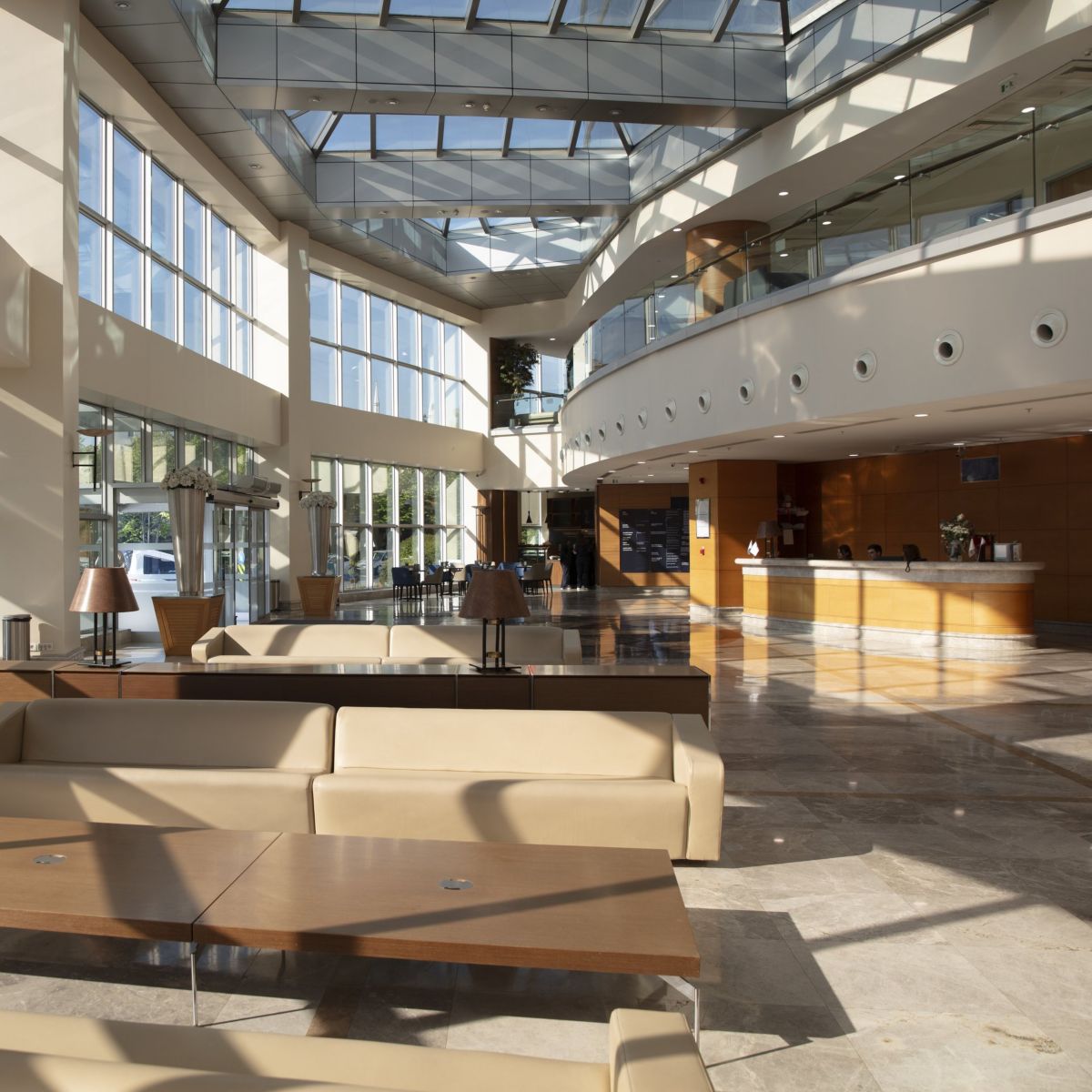 A sunlit, high-ceilinged corporate office lobby featuring modern furniture and glass atrium architecture.