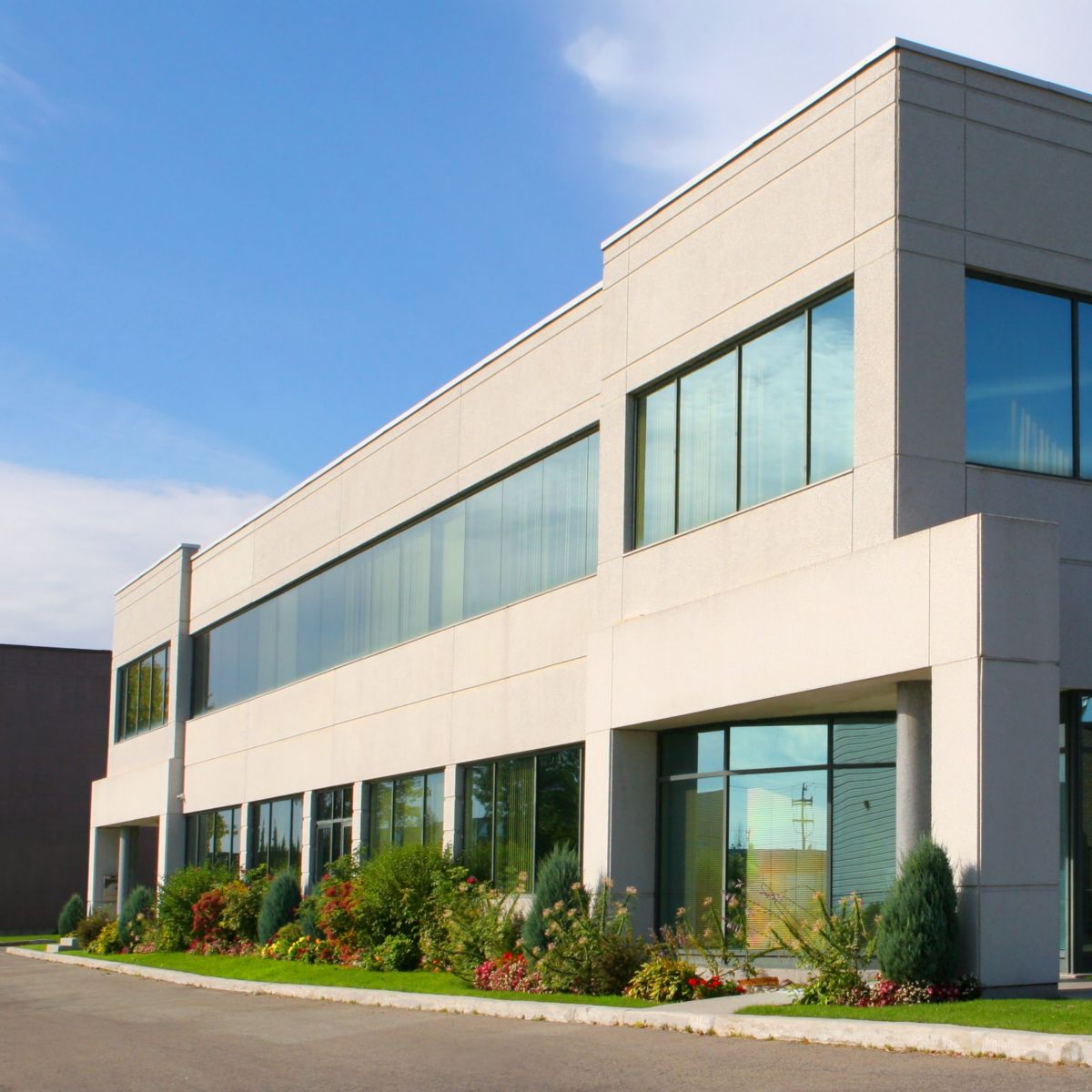 A contemporary low-rise corporate office building featuring glass curtain walls, precast concrete panels, and manicured landscaping under a blue sky.