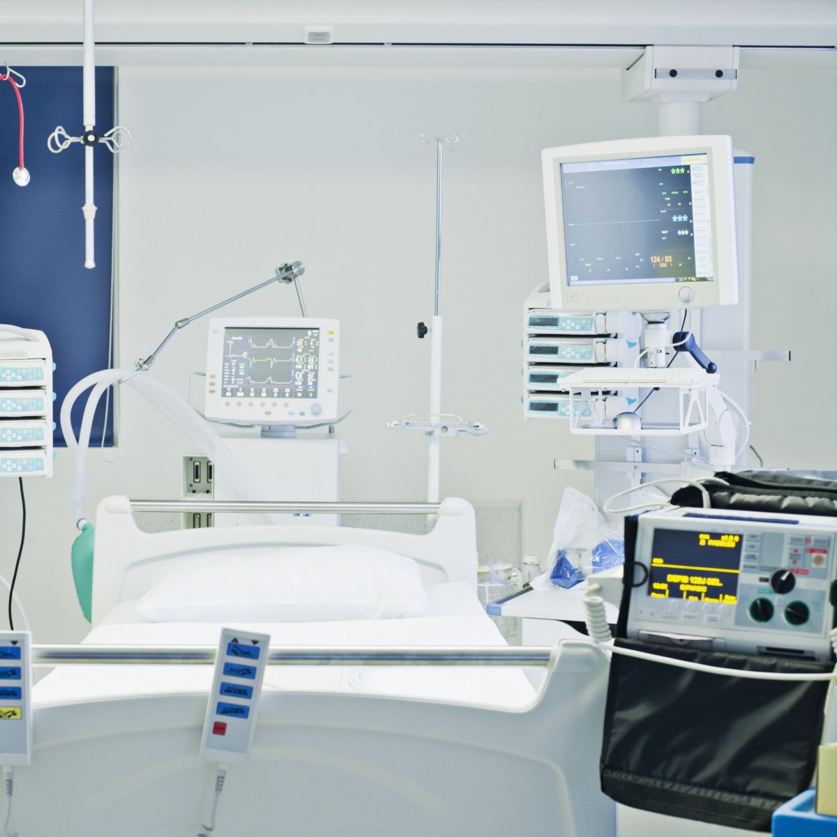 A clean hospital room featuring a high-tech patient bed surrounded by advanced medical monitoring equipment and life-support systems.