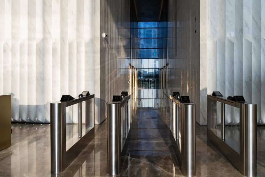 A symmetric view of sleek, stainless steel turnstiles in a minimalist marble lobby.