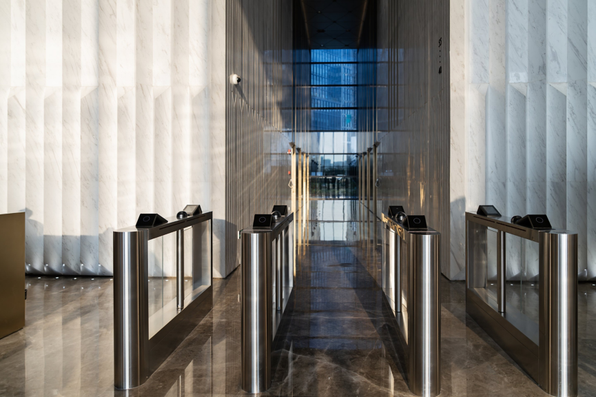 A symmetric view of sleek, stainless steel turnstiles in a minimalist marble lobby.