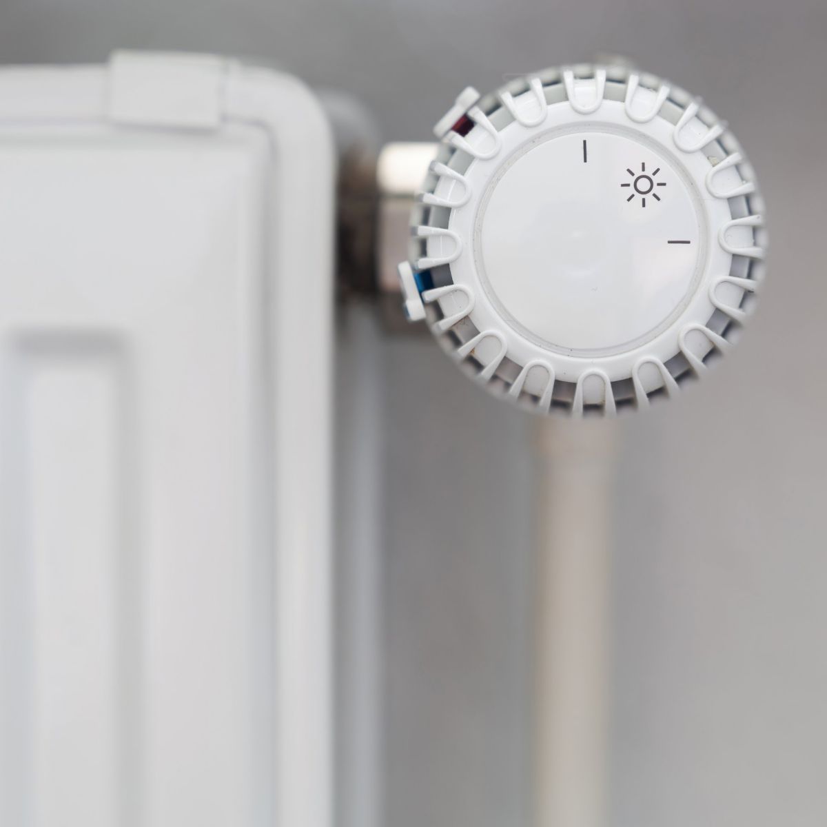 A close-up view of a white modern radiator thermostatic valve set against a neutral blurred background in a corporate interior setting.