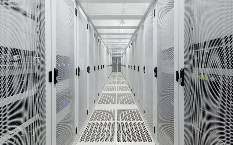 A symmetrical view down a bright, white data center aisle featuring rows of high-security perforated metal server cabinets.