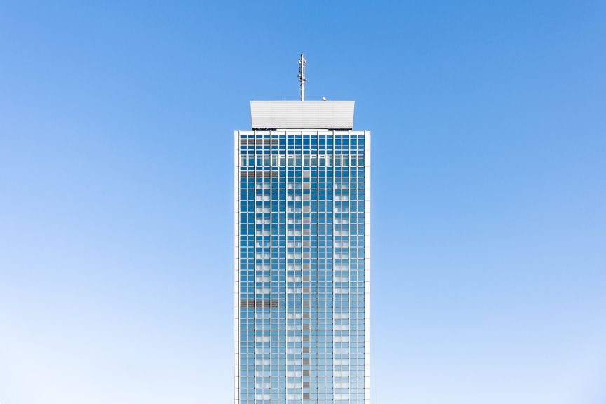 A symmetrical, low-angle shot of a glass skyscraper tower centered against a clear blue sky.