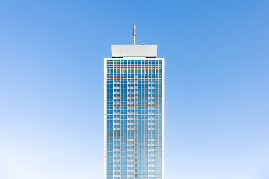 A symmetrical, low-angle shot of a glass skyscraper tower centered against a clear blue sky.