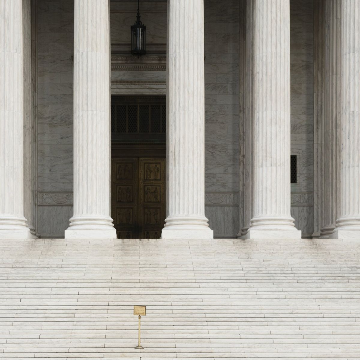 A symmetrical, eye-level shot captures the grand marble staircase and towering fluted columns of a historic institutional building facade.