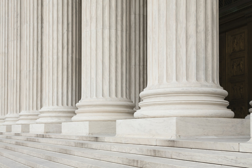 A close-up view of towering marble columns and stone steps at the entrance of a monumental neoclassical building, symbolizing justice and architectural strength.