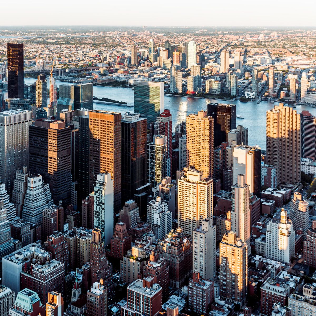 An elevated sunset view of Manhattan skyscrapers illuminated by golden light against the East River.