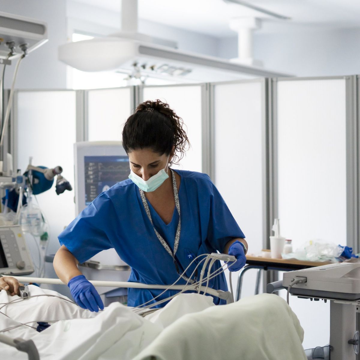 A focused nurse in protective gear monitors a critically ill patient using medical equipment in a modern hospital intensive care unit.