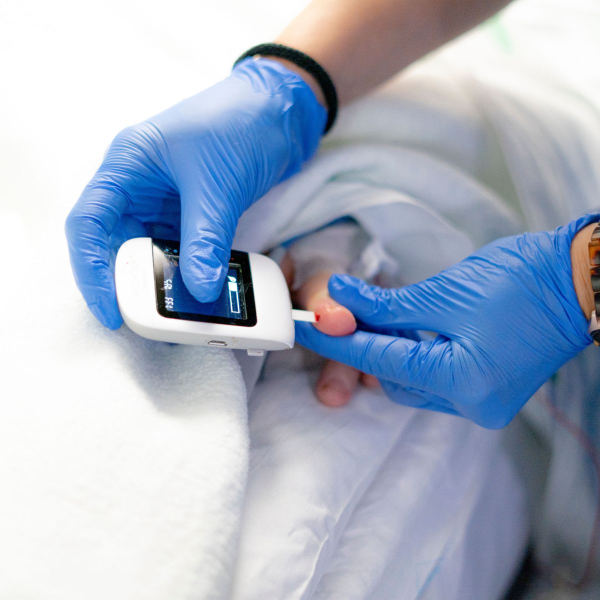 Close-up of gloved hands using a handheld device to test a blood sample from a finger.