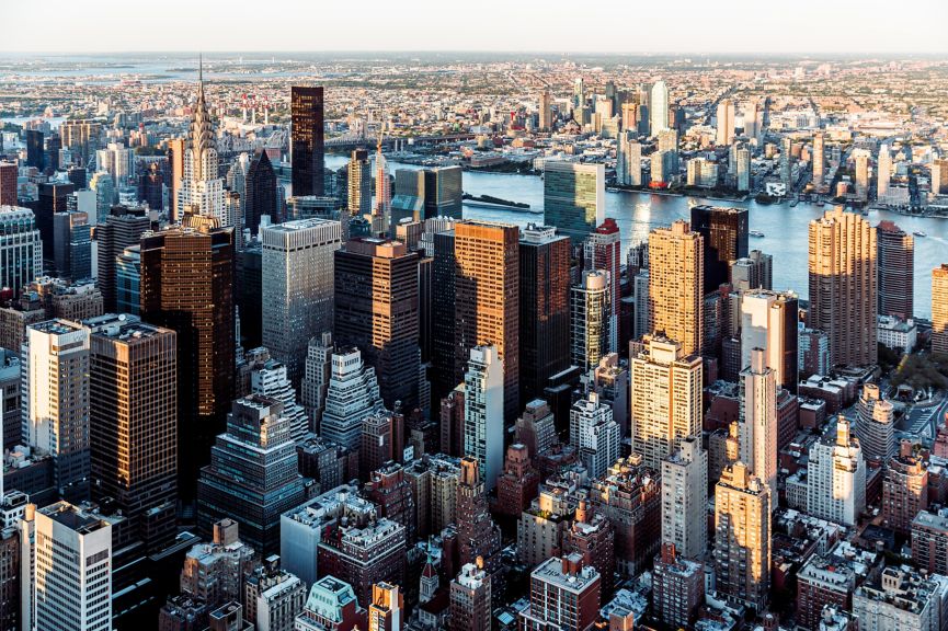 An elevated aerial view captures the sunlit midtown Manhattan skyline and East River during the vibrant golden hour.