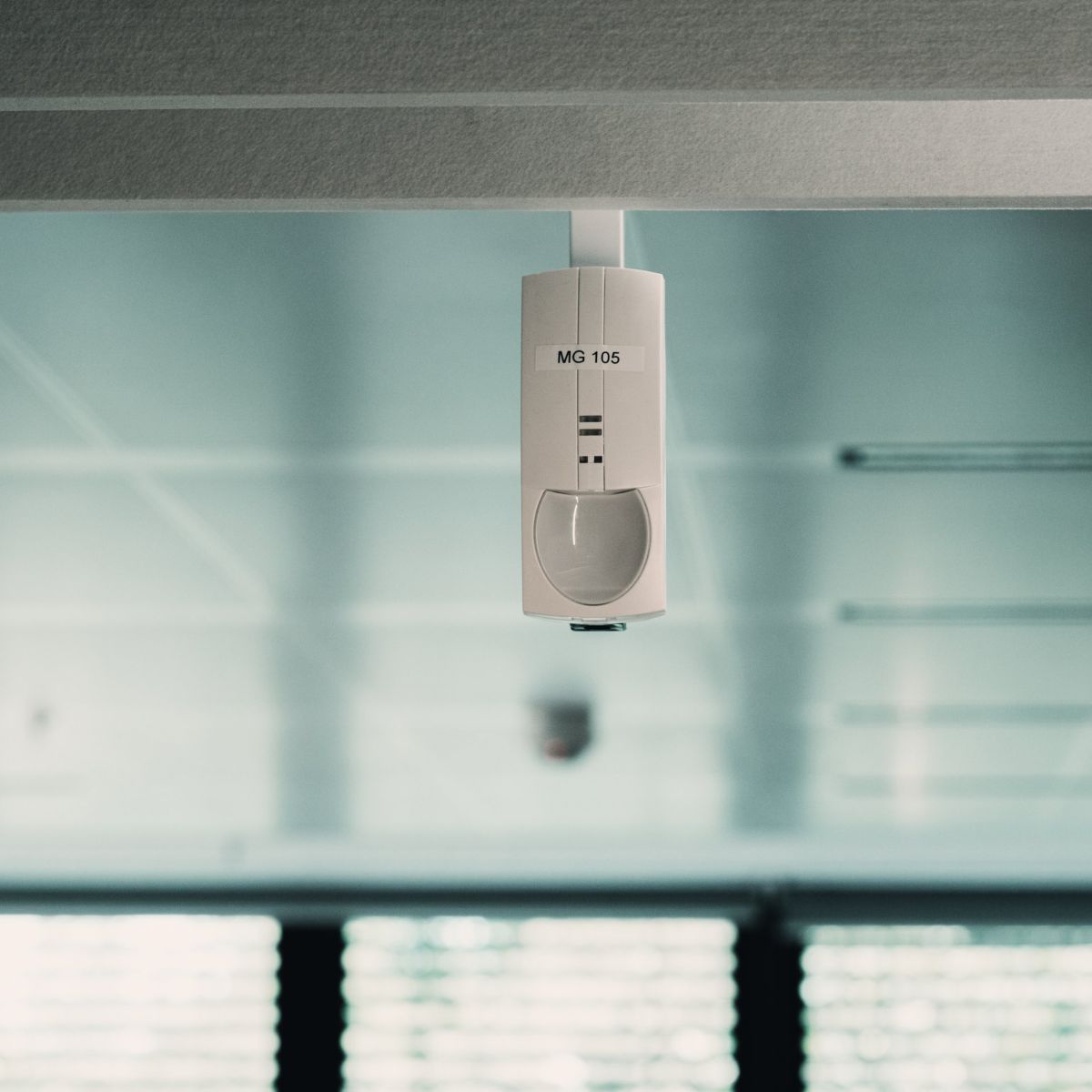 An indoor ceiling-mounted motion sensor labeled MG 105 installed in a modern office environment.